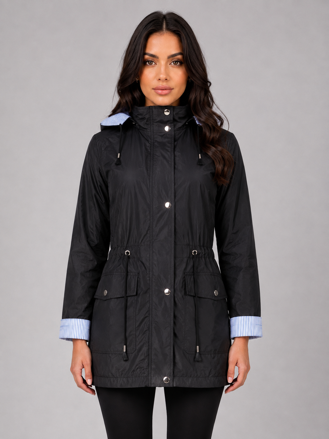 Woman wearing black lightweight water resistant hooded rain jacket with blue striped collar and cuffs, front buttoned closure