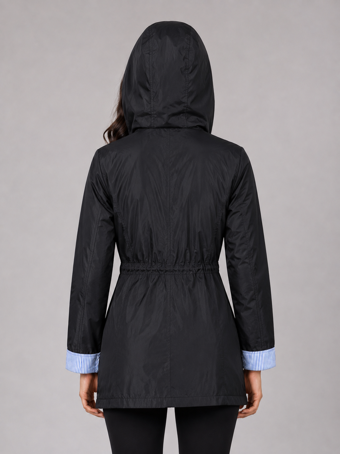 Woman wearing black lightweight water-resistant hooded rain jacket with blue striped cuffs, shown from back view