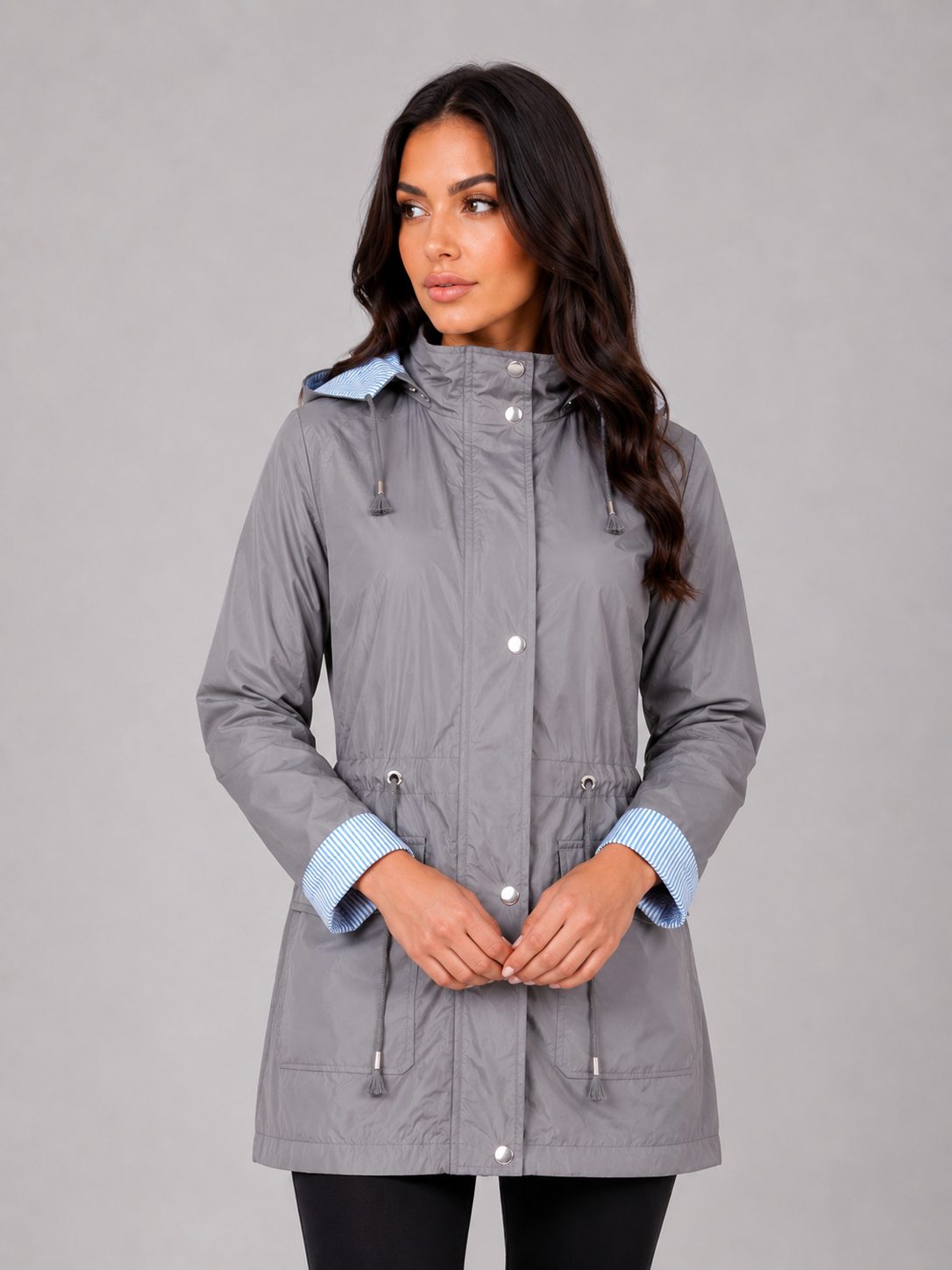 Woman wearing gray lightweight water resistant hooded rain jacket with light blue striped cuffs and buttons