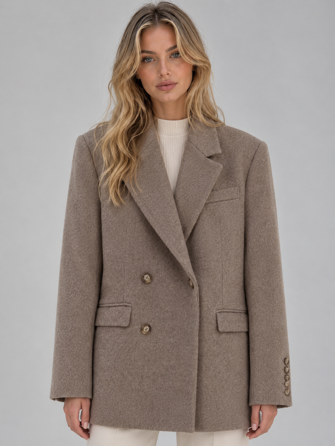 Woman wearing a beige tailored longline double-breasted blazer jacket with notch lapels over a cream ribbed top
