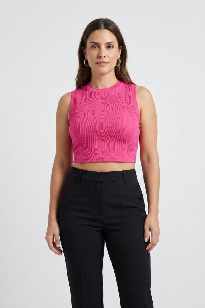 Woman wearing bright pink ribbed sleeveless crop top with round neckline and high-waisted black trousers