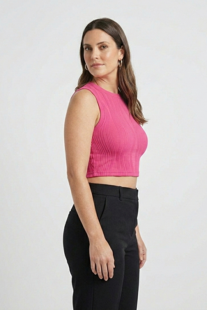 Woman wearing a pink ribbed sleeveless crop top with high neckline and black pants, standing against a white background