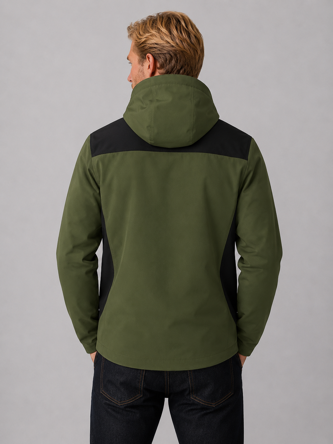 Man wearing olive green and black hooded windbreaker jacket with dark jeans, viewed from back