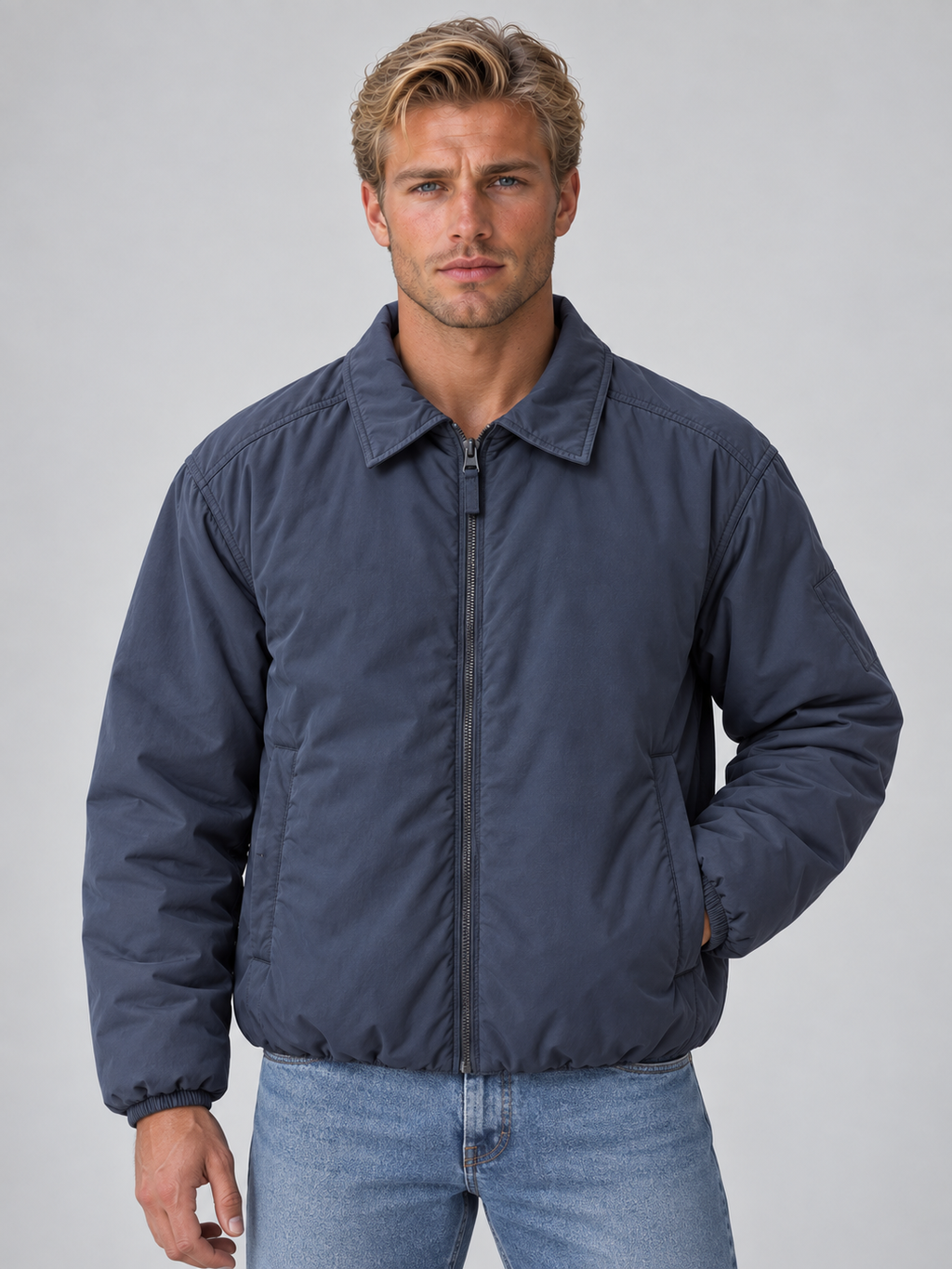 Man wearing navy blue lightweight padded bomber jacket with collar and full zip over light blue jeans