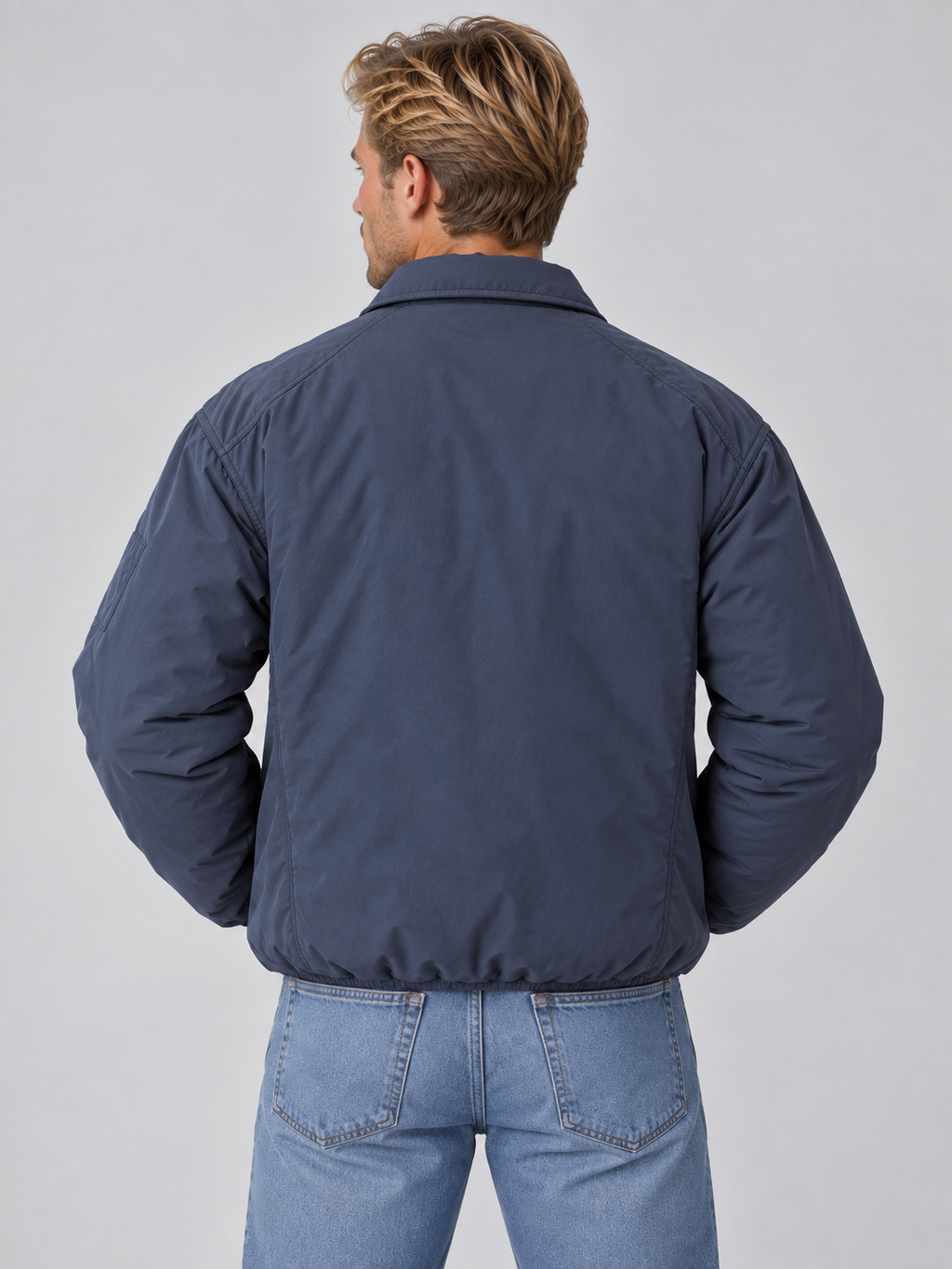 Man wearing navy blue lightweight padded bomber jacket with collared neckline and full zip closure, styled with light blue jeans