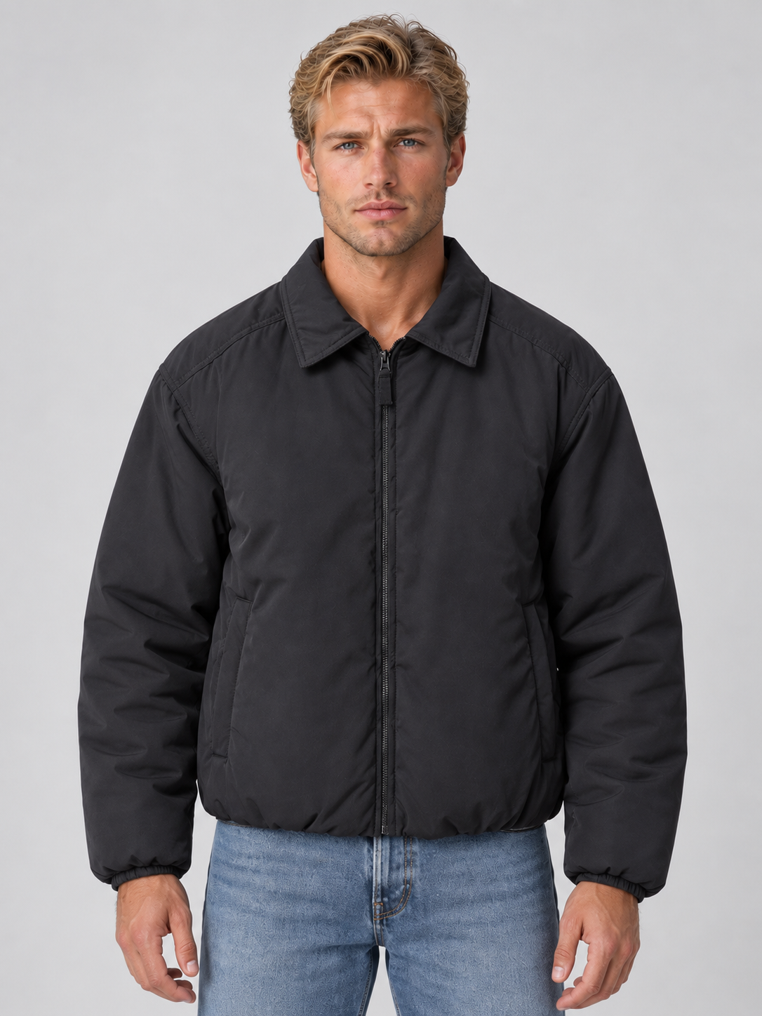 Man wearing black lightweight padded bomber jacket with collar and full zip over blue jeans, front view