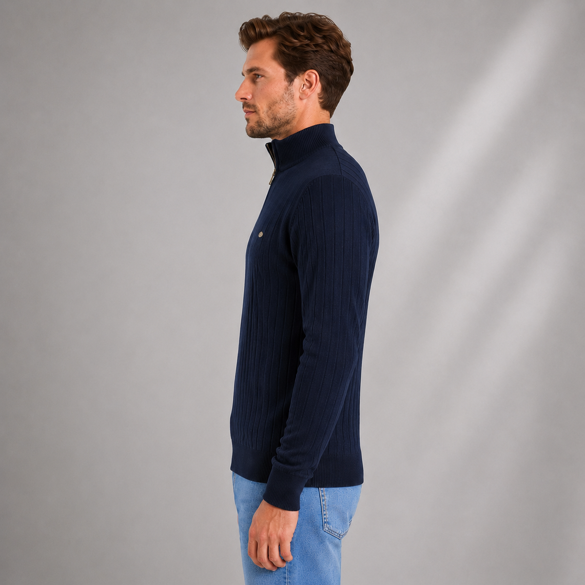 Man wearing navy ribbed funnel neck quarter zip jumper with light blue jeans against neutral background