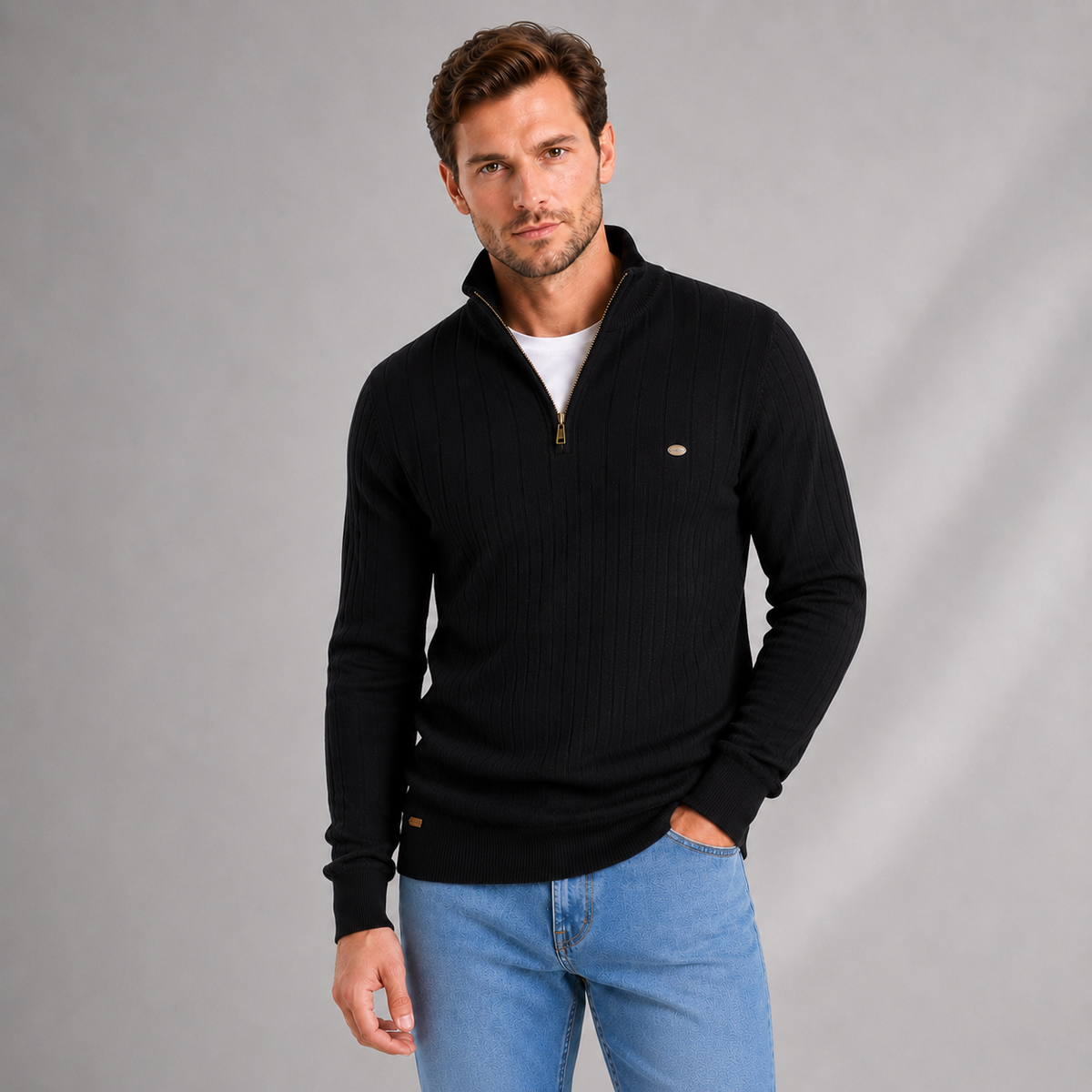 Man wearing black ribbed quarter zip jumper with white undershirt and blue jeans against gray background
