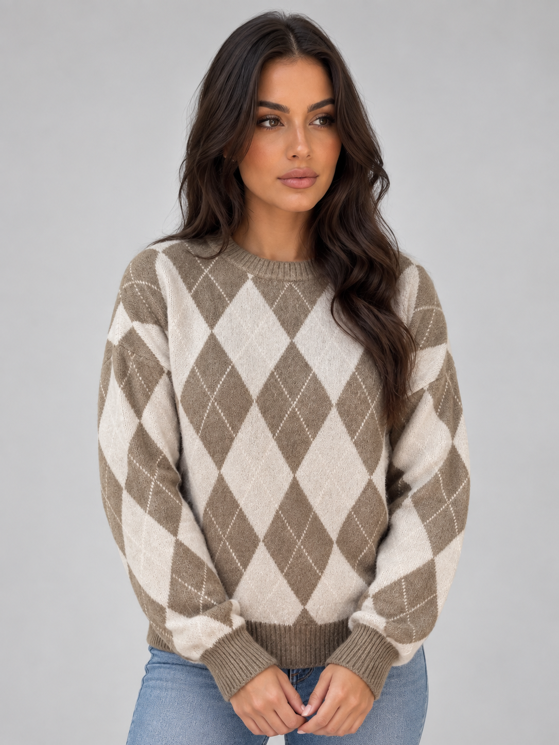 Woman wearing tan and cream argyle knit crew neck sweater with blue jeans against gray background