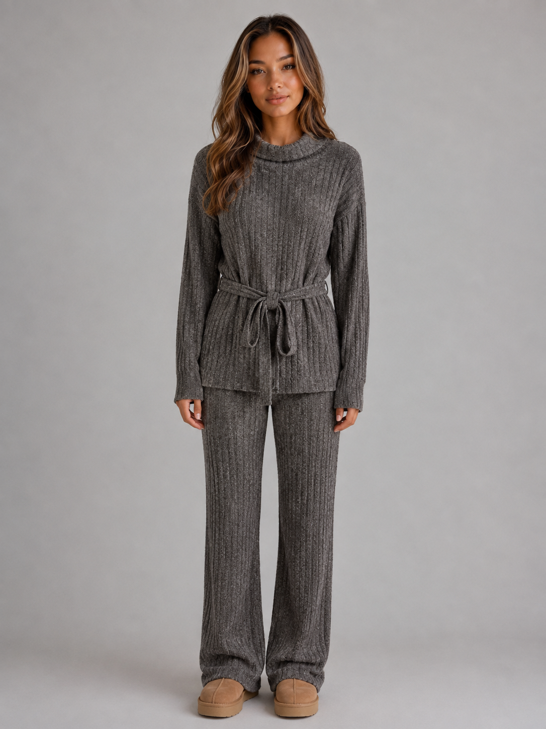 Woman wearing gray ribbed knit roll neck sweater with drawstring waist paired with matching wide leg knit trousers and tan platform slippers
