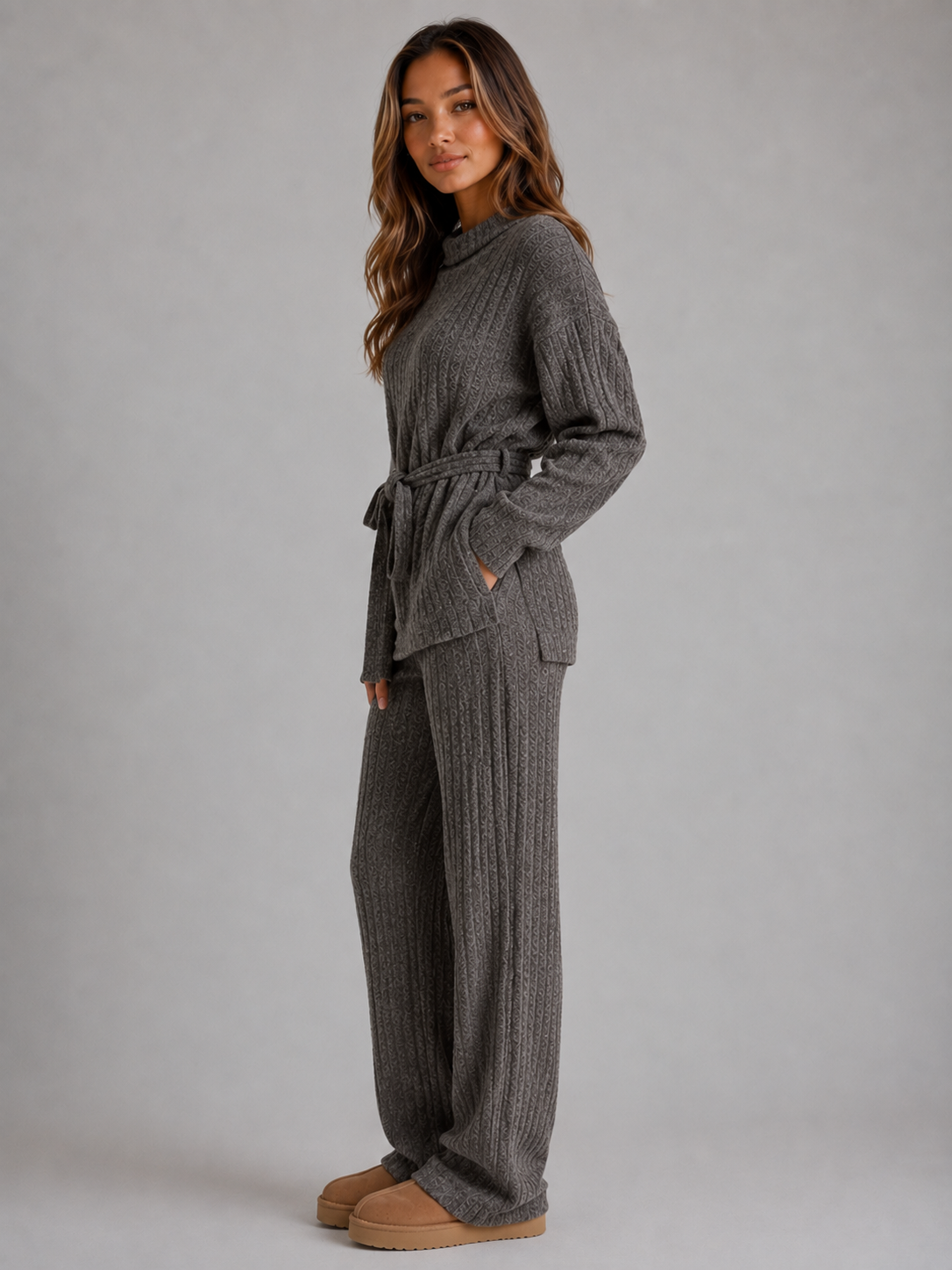Woman wearing charcoal grey ribbed knit roll neck jumper with tie belt and matching wide leg knit trousers, styled with tan platform boots
