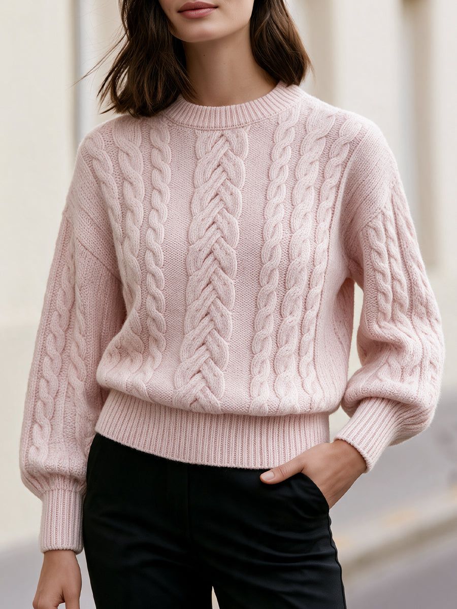 Woman wearing pink cropped cable-knit sweater with crew neck and drop shoulders, paired with black pants