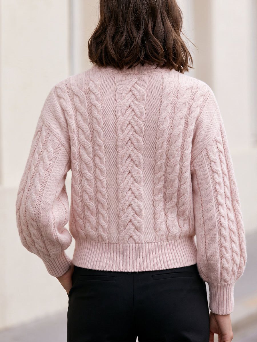 Woman wearing pink cropped cable-knit sweater with drop shoulders and crew neckline, viewed from back, paired with black pants