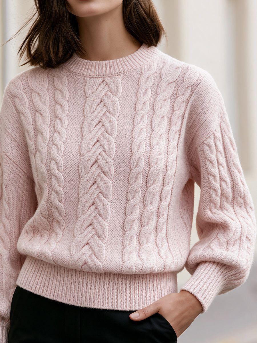 Woman wearing light pink cropped cable-knit sweater with crew neck and drop shoulders over black pants