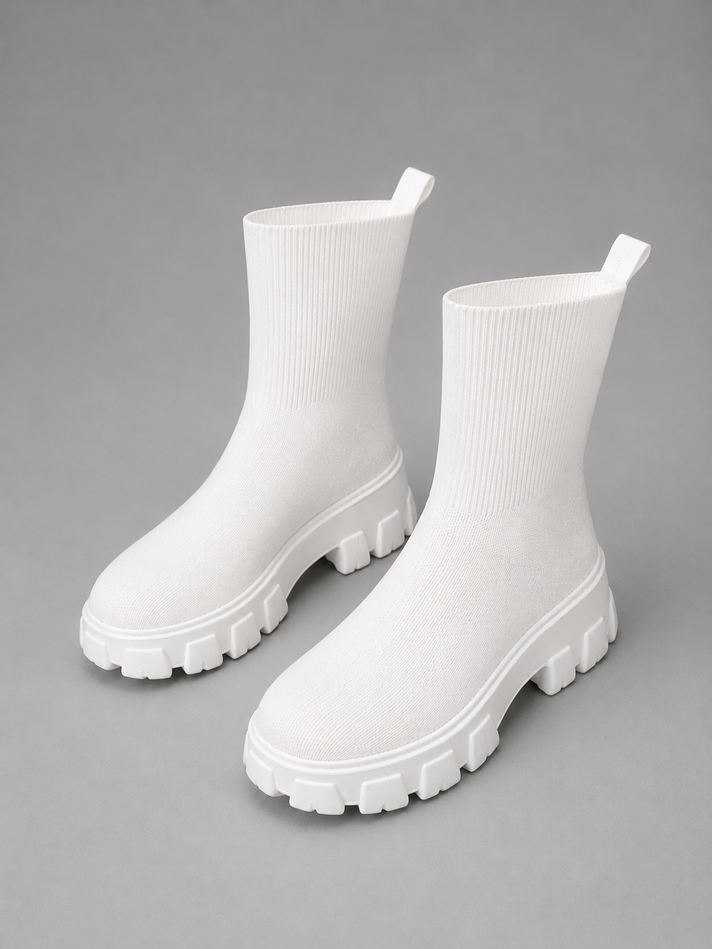 White chunky sole stretch sock boots with ribbed knit upper and oversized lug tread sole on gray background