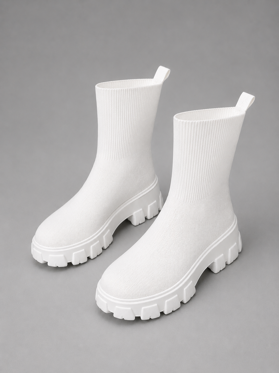 White chunky sole stretch sock boots with ribbed knit upper and oversized lug tread sole on gray background