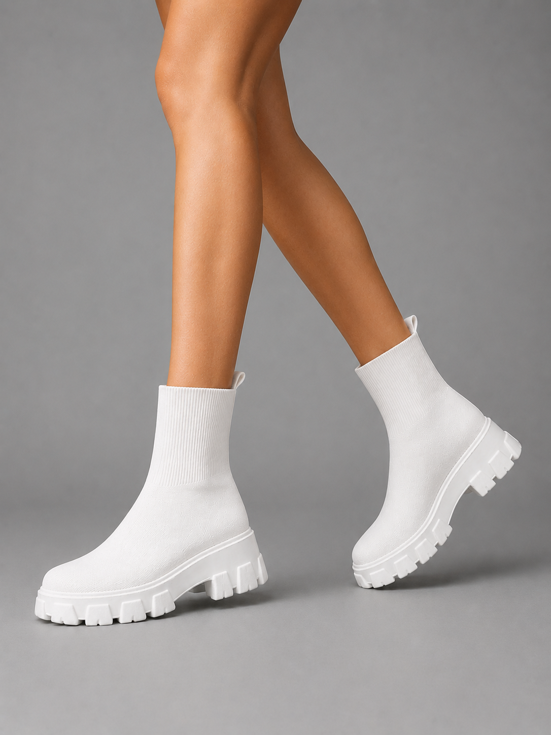 Woman wearing white chunky sole stretch sock boots with ribbed texture and lug tread on gray background