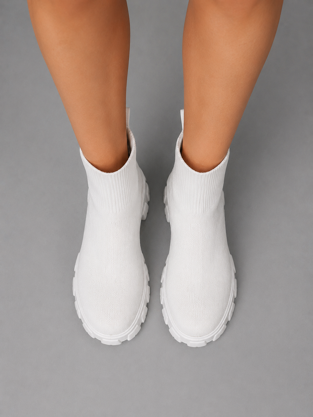 Woman wearing white chunky sole stretch sock boots with ribbed knit fabric and lug sole, viewed from above on gray background