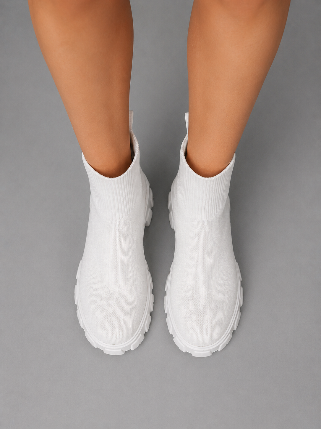 Woman wearing white chunky sole stretch sock boots with ribbed knit fabric and lug sole, viewed from above on gray background
