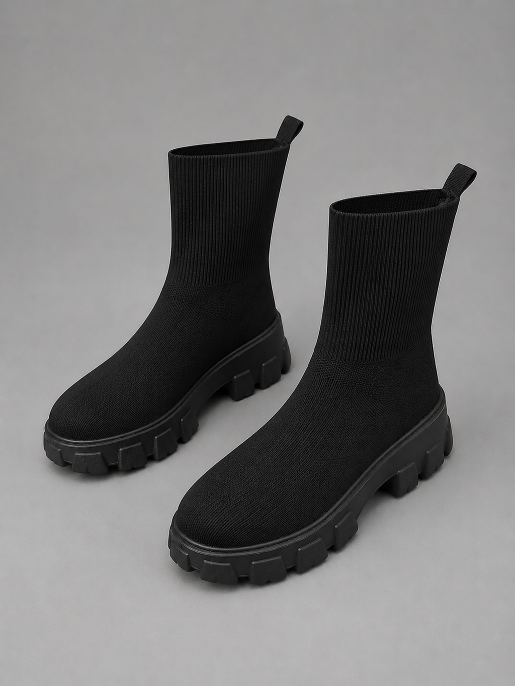 Black stretch sock boots with chunky lug soles and pull tabs, displayed on gray background