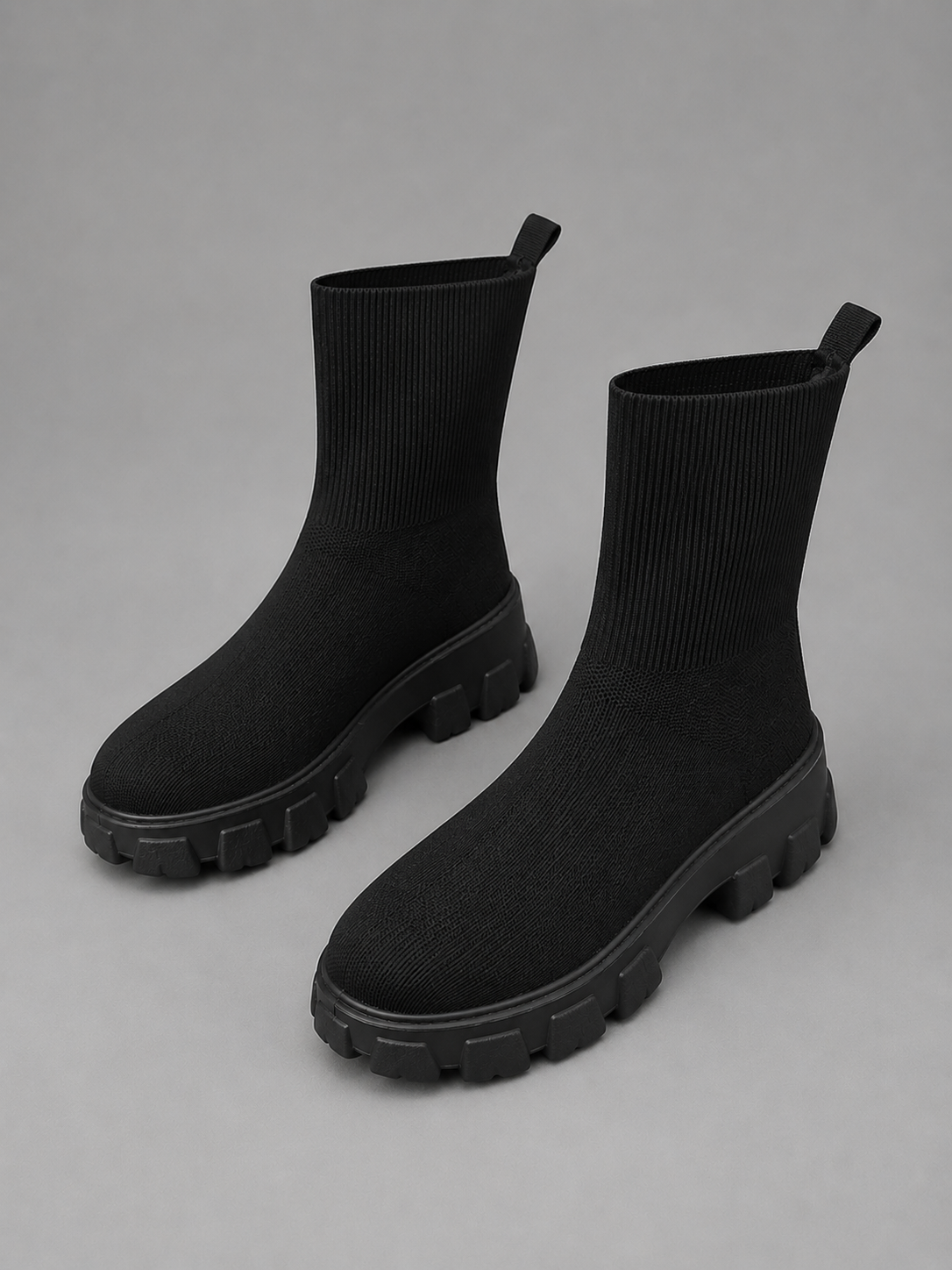 Black stretch sock boots with chunky lug soles and pull tabs, displayed on gray background