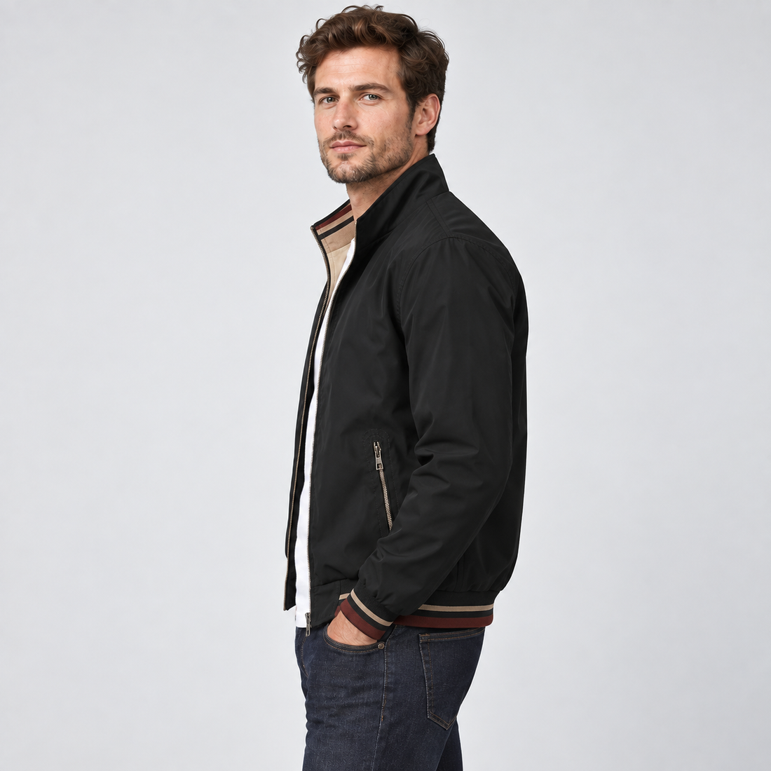 Man wearing black reversible zip-up bomber jacket with beige interior and striped trim, styled with dark jeans