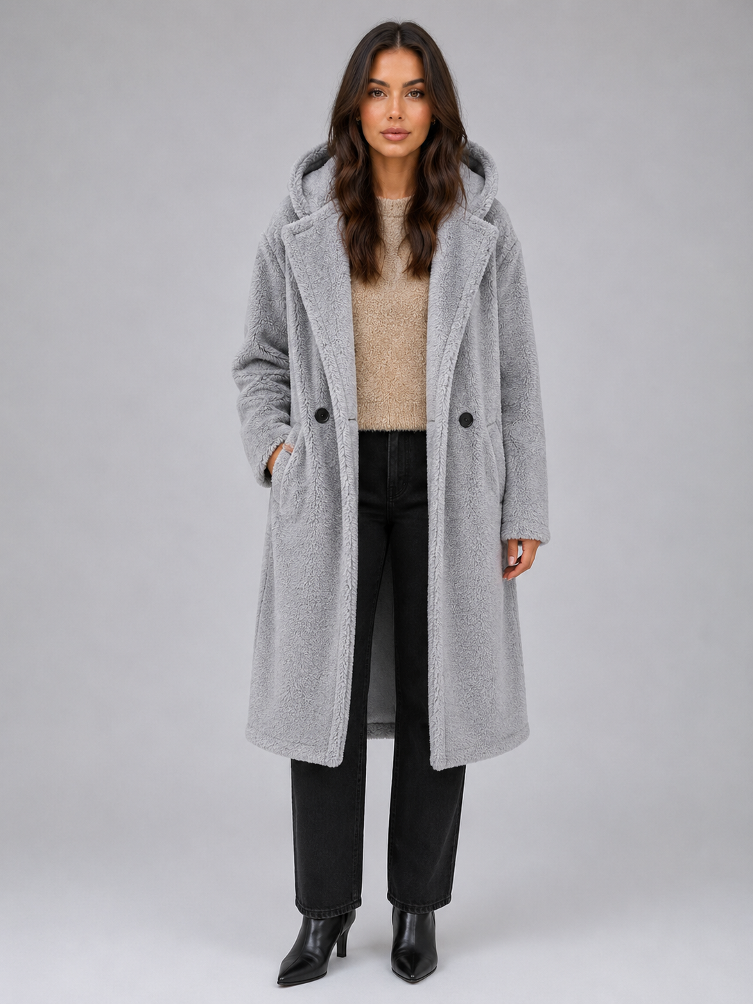 Woman wearing oversized light gray hooded borg teddy coat over beige sweater and black jeans with black boots