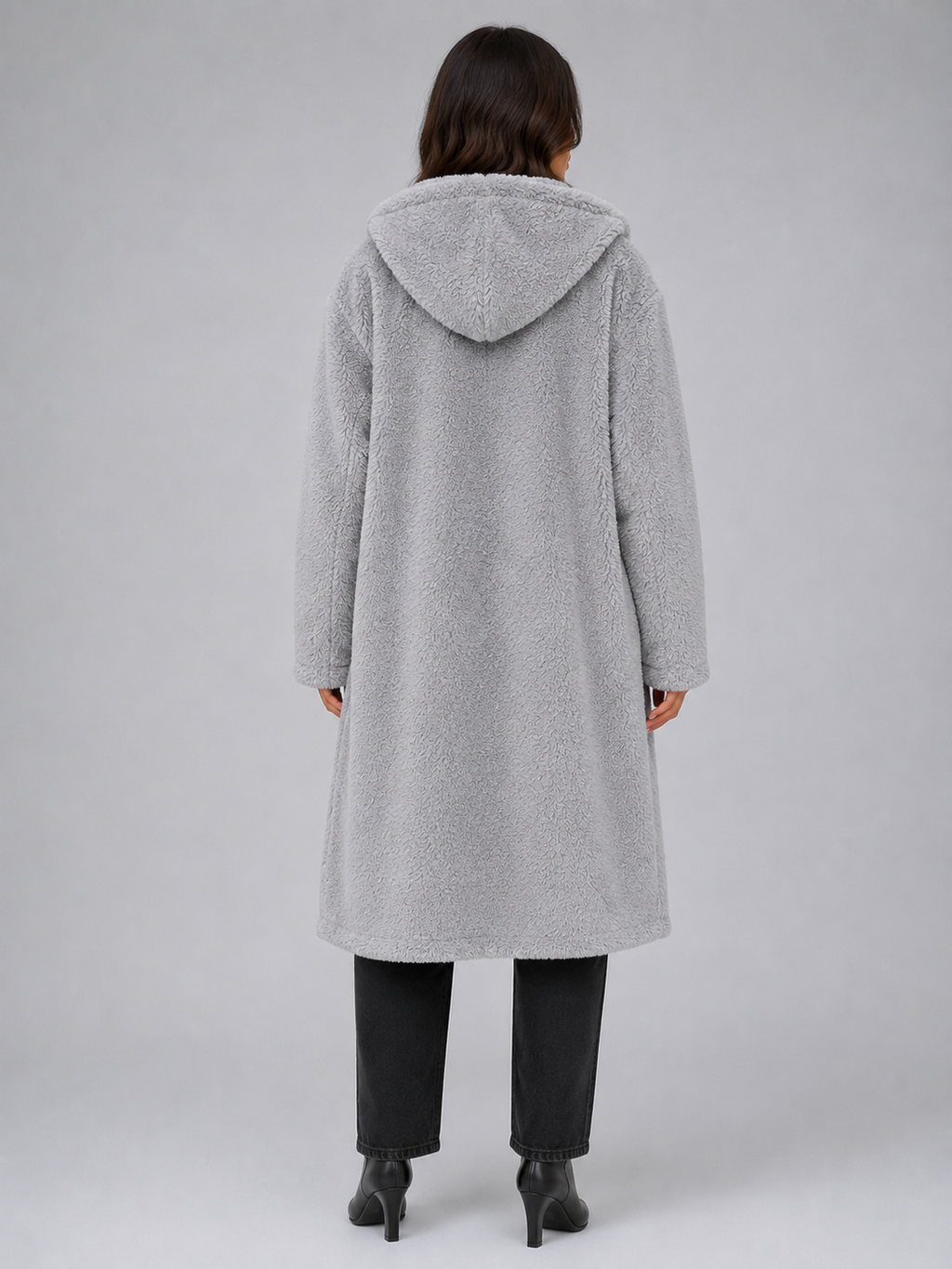 Woman wearing light gray oversized long hooded borg teddy coat over black jeans and black heeled boots, back view