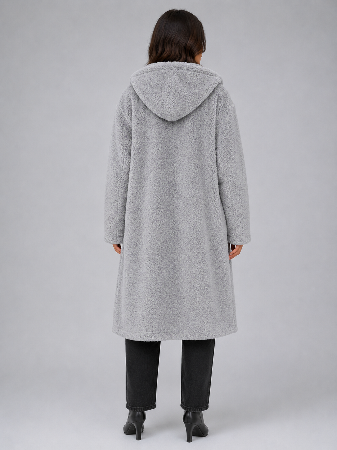 Woman wearing light gray oversized long hooded borg teddy coat over black jeans and black heeled boots, back view
