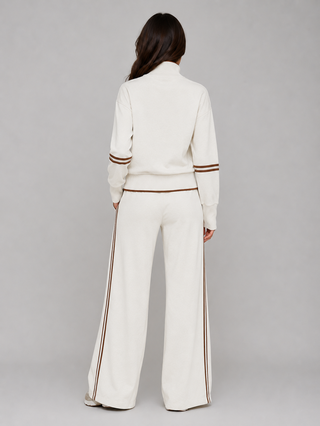 Woman wearing cream half zip cropped jacket and wide leg pants with brown striping details, shown from back view