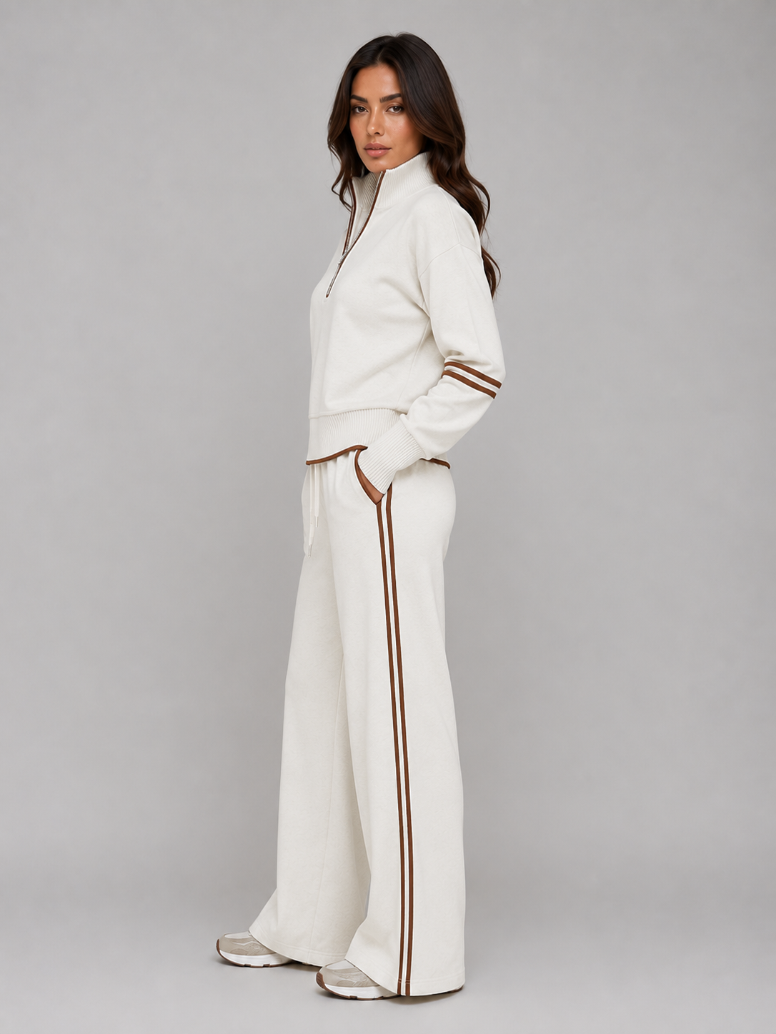 Woman wearing cream relaxed wide leg tracksuit with brown stripe trim, half zip sweatshirt and matching lounge pants
