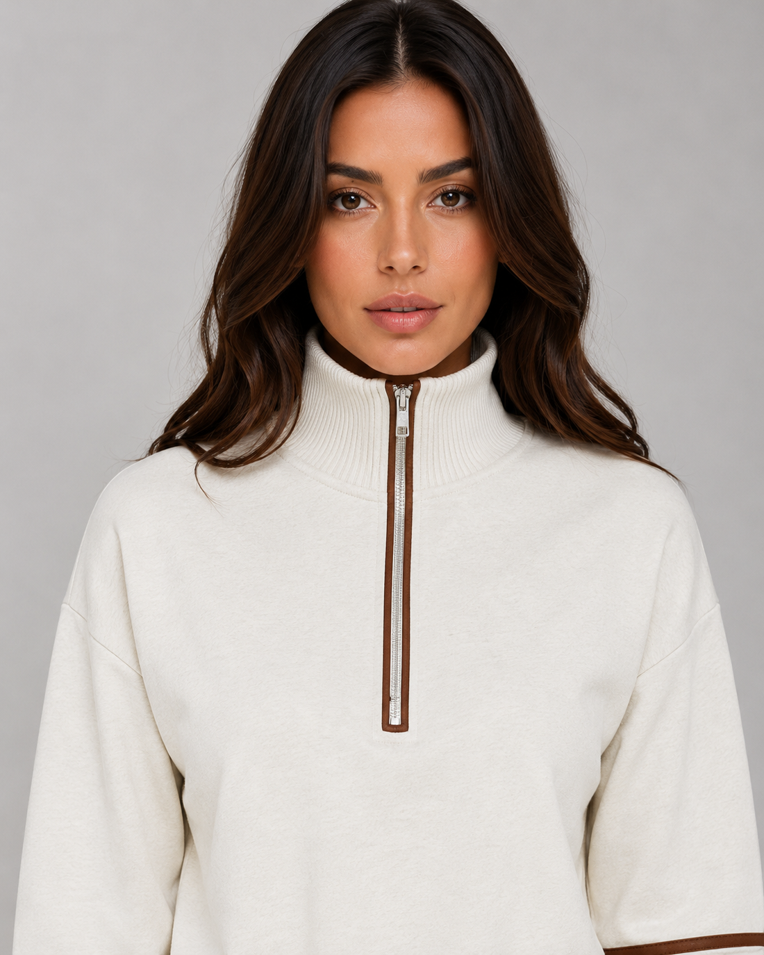 Woman wearing cream relaxed wide leg tracksuit with brown half zip collar and ribbed neckline against gray background