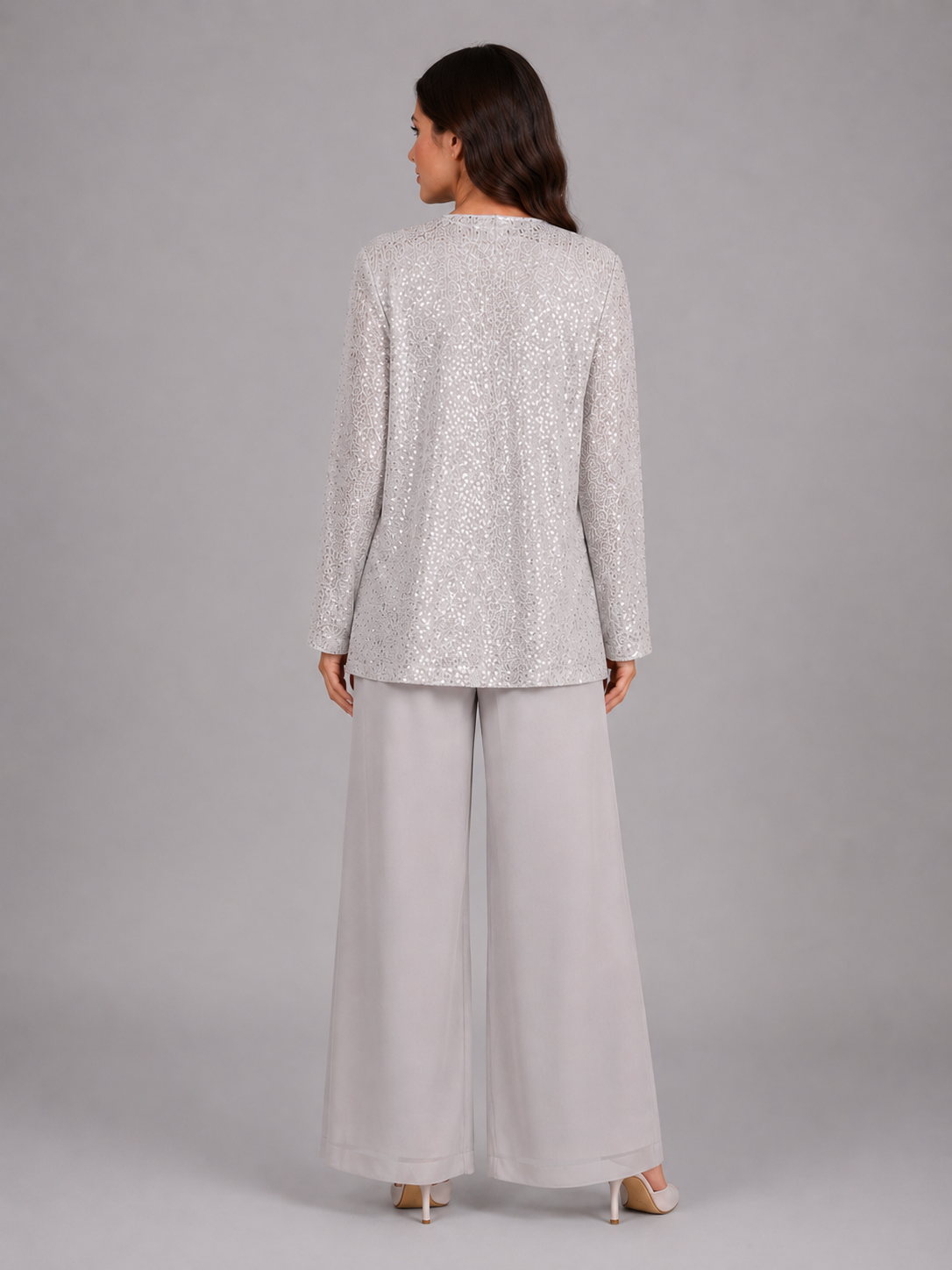 Woman wearing silver sequin long-sleeve top with white wide-leg trousers, shown from back view against gray background