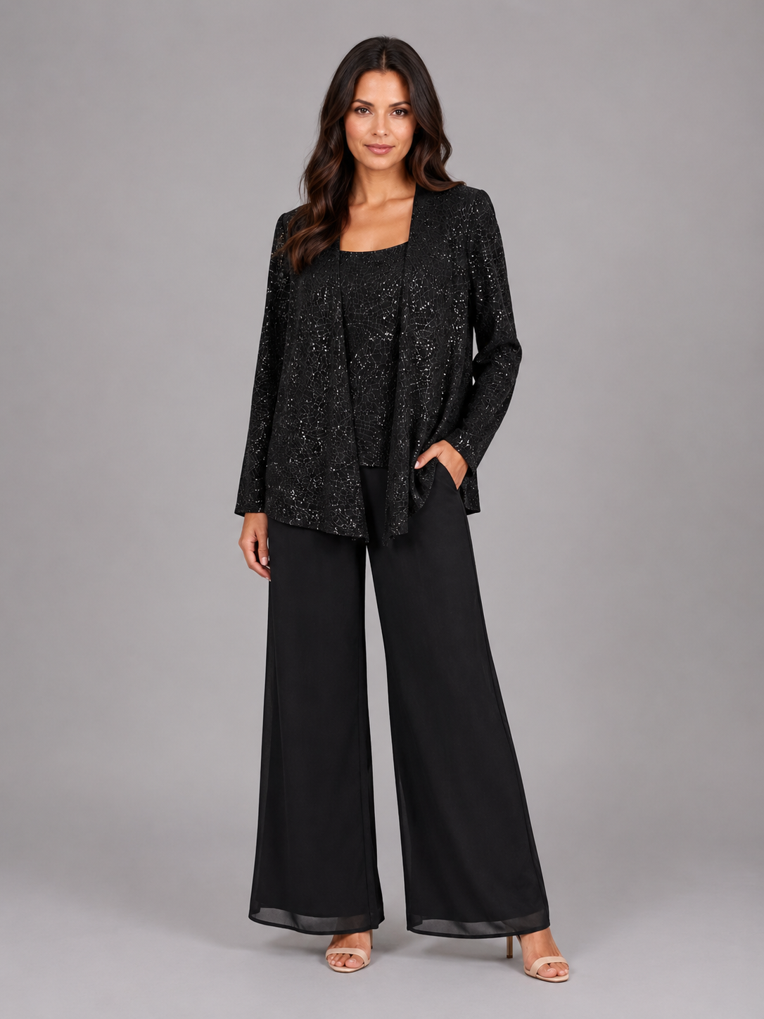 Woman wearing black sequin cardigan with matching tank top and wide-leg trousers, styled with nude sandals against gray background