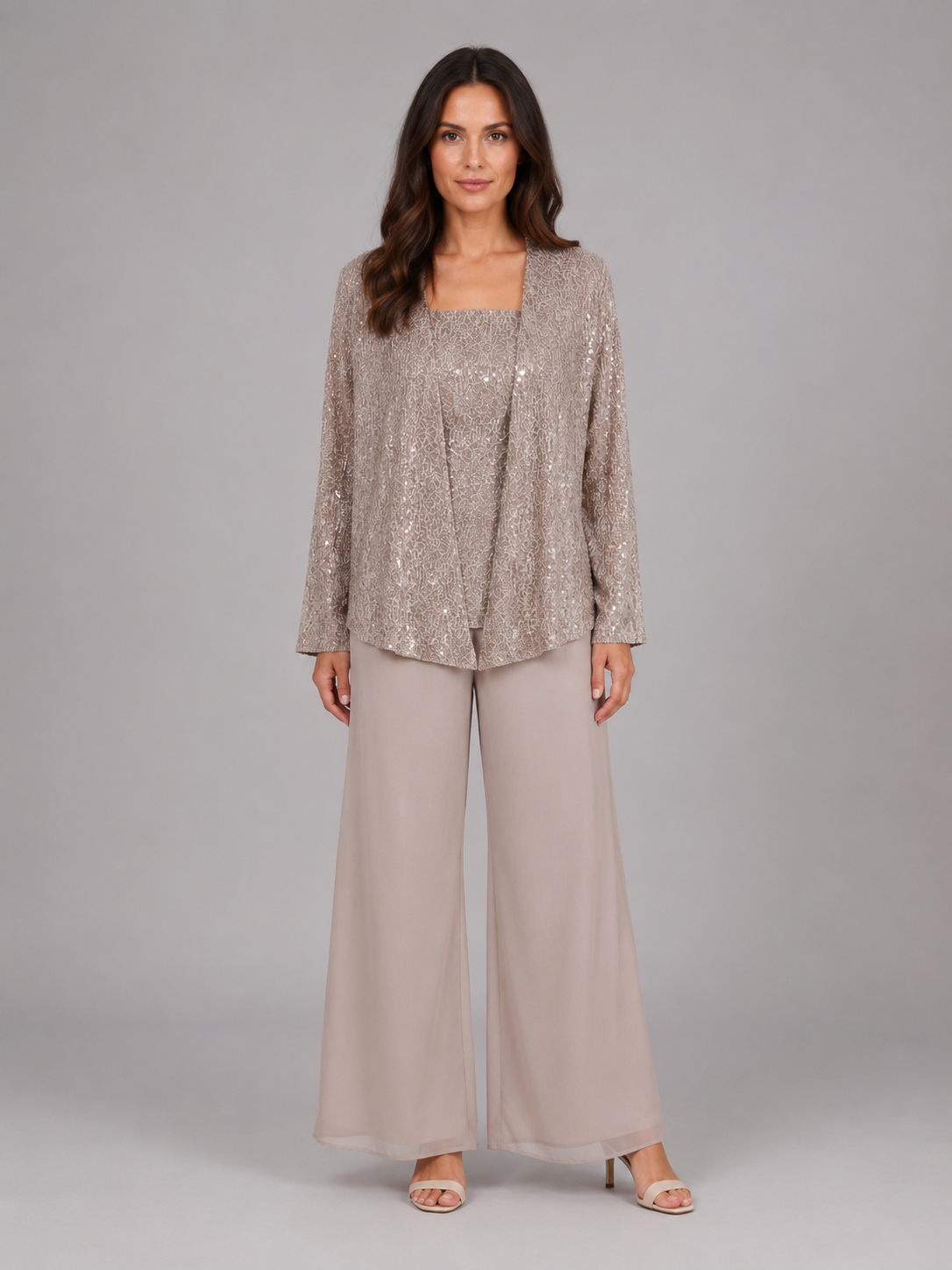 Woman wearing champagne sequin cardigan with square neckline and matching wide-leg chiffon trousers, styled with nude heels