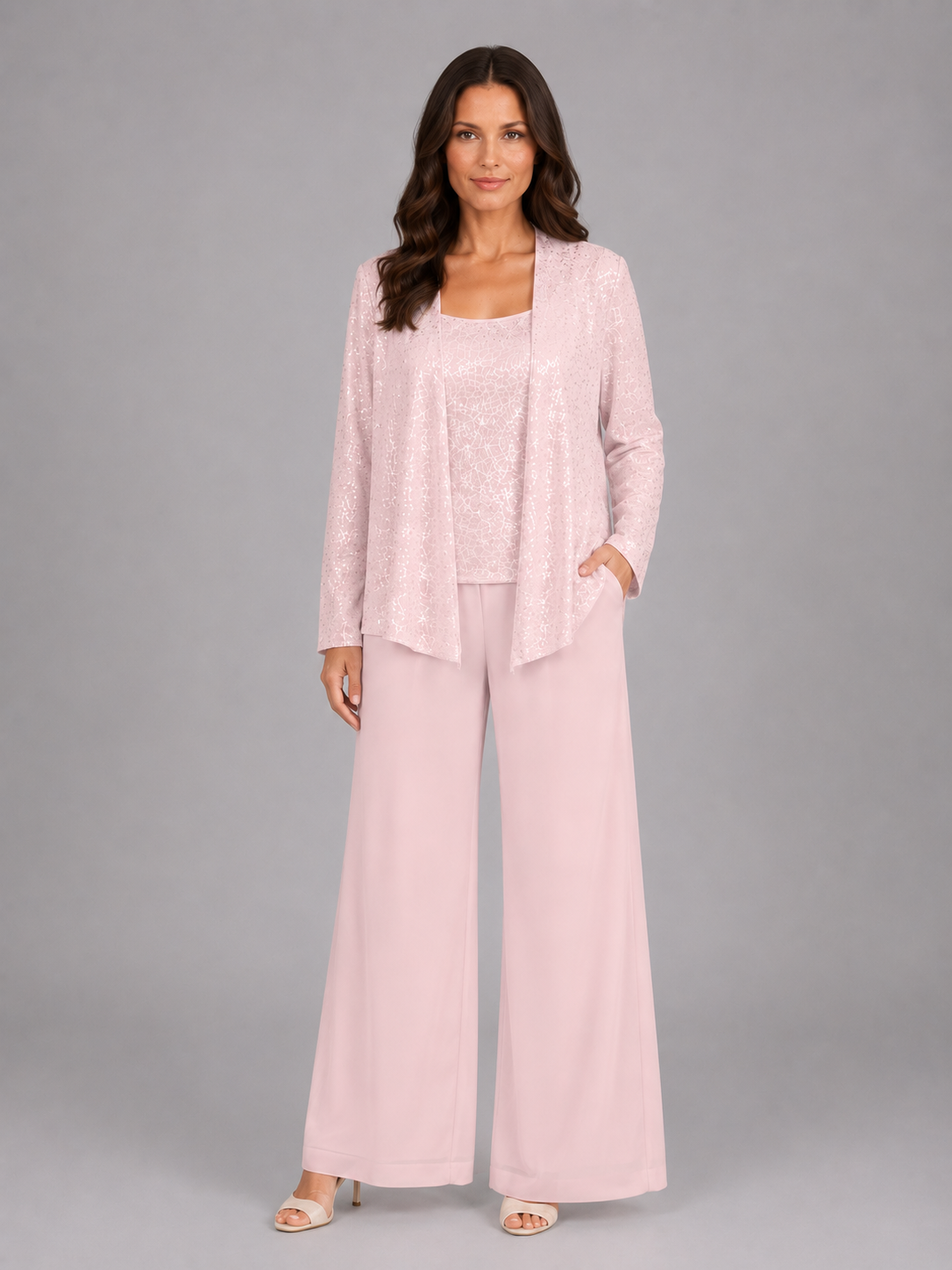 Woman wearing pink sequin three-piece trouser set with long cardigan, tank top, and wide-leg pants on gray background