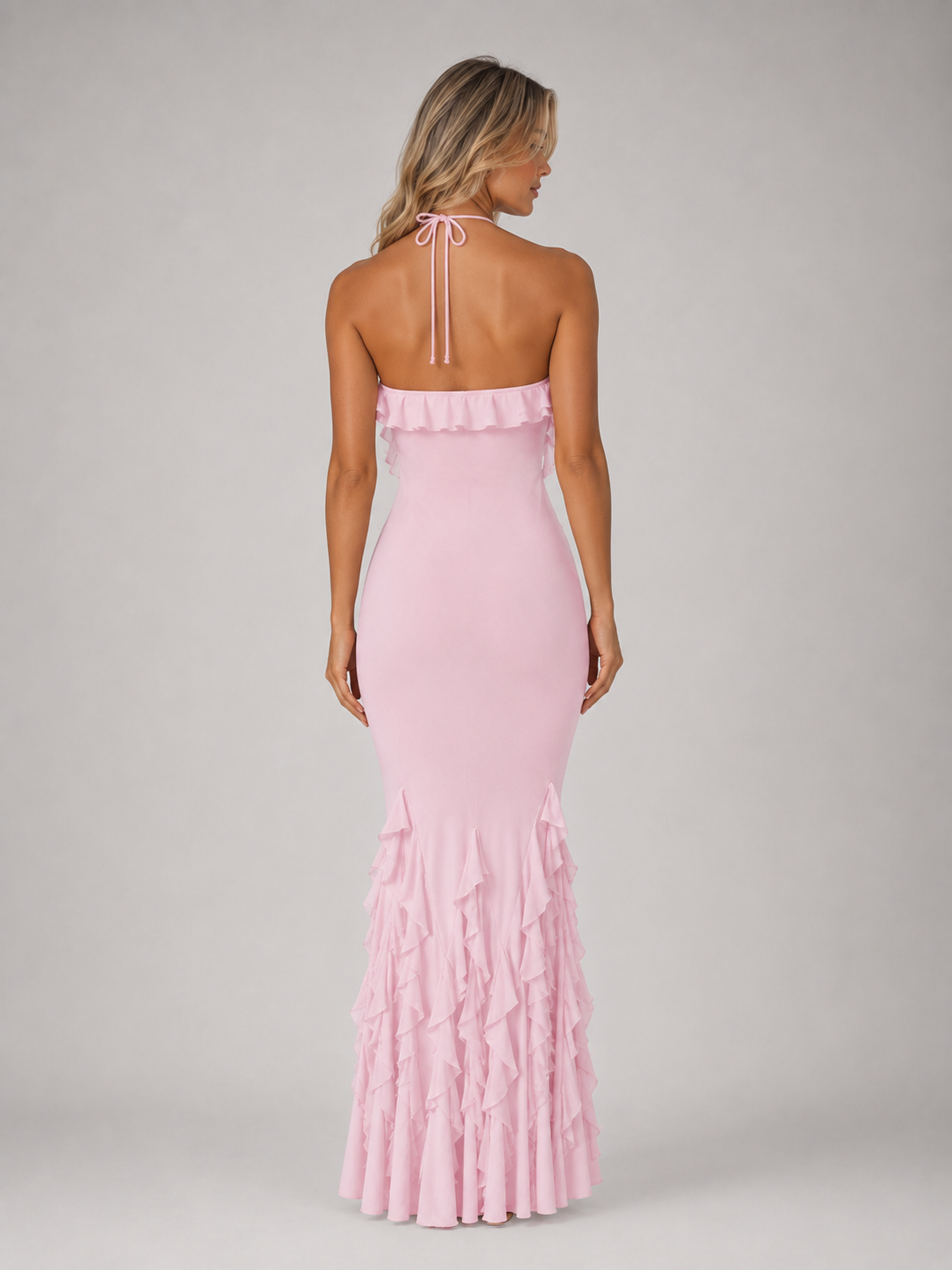 Woman wearing pink halterneck bodycon maxi gown with ruffled fishtail hem, shown from back view against white background
