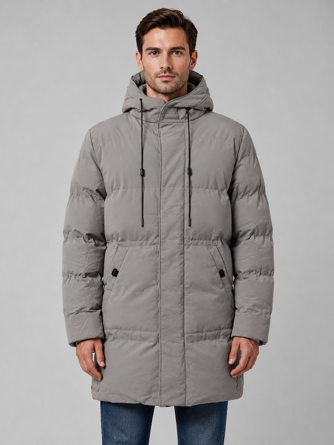 Man wearing beige longline hooded padded parka jacket with black drawstrings and hand pockets over jeans