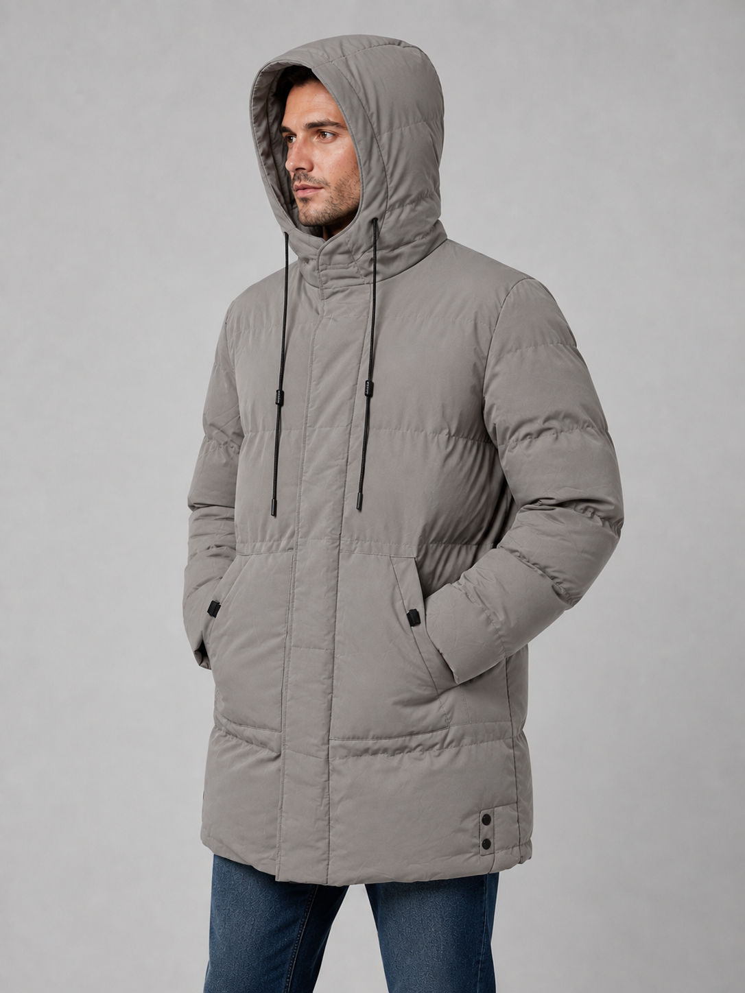 Man wearing gray longline hooded padded winter parka jacket with hands in pockets over blue jeans