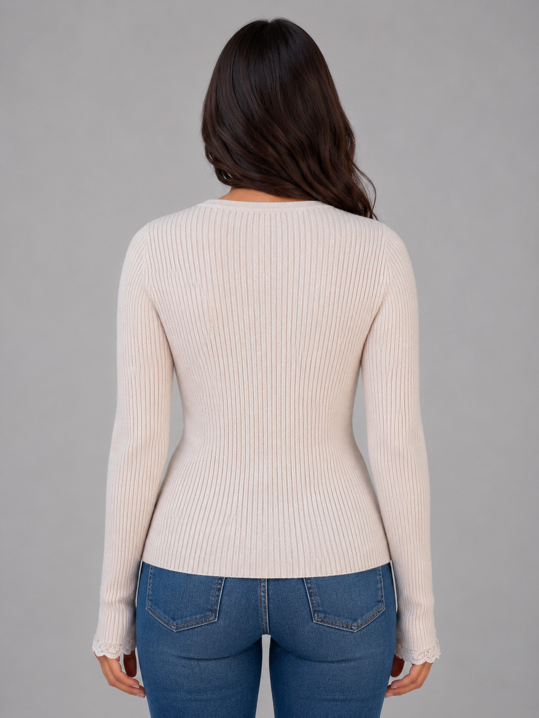 Woman wearing cream ribbed knit cardigan with lace cuffs and blue jeans, back view