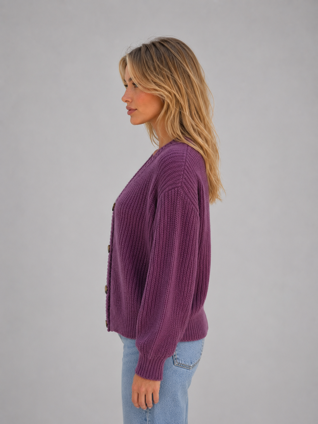 Woman wearing purple chunky knit button front V-neck cardigan with light blue jeans, side profile view