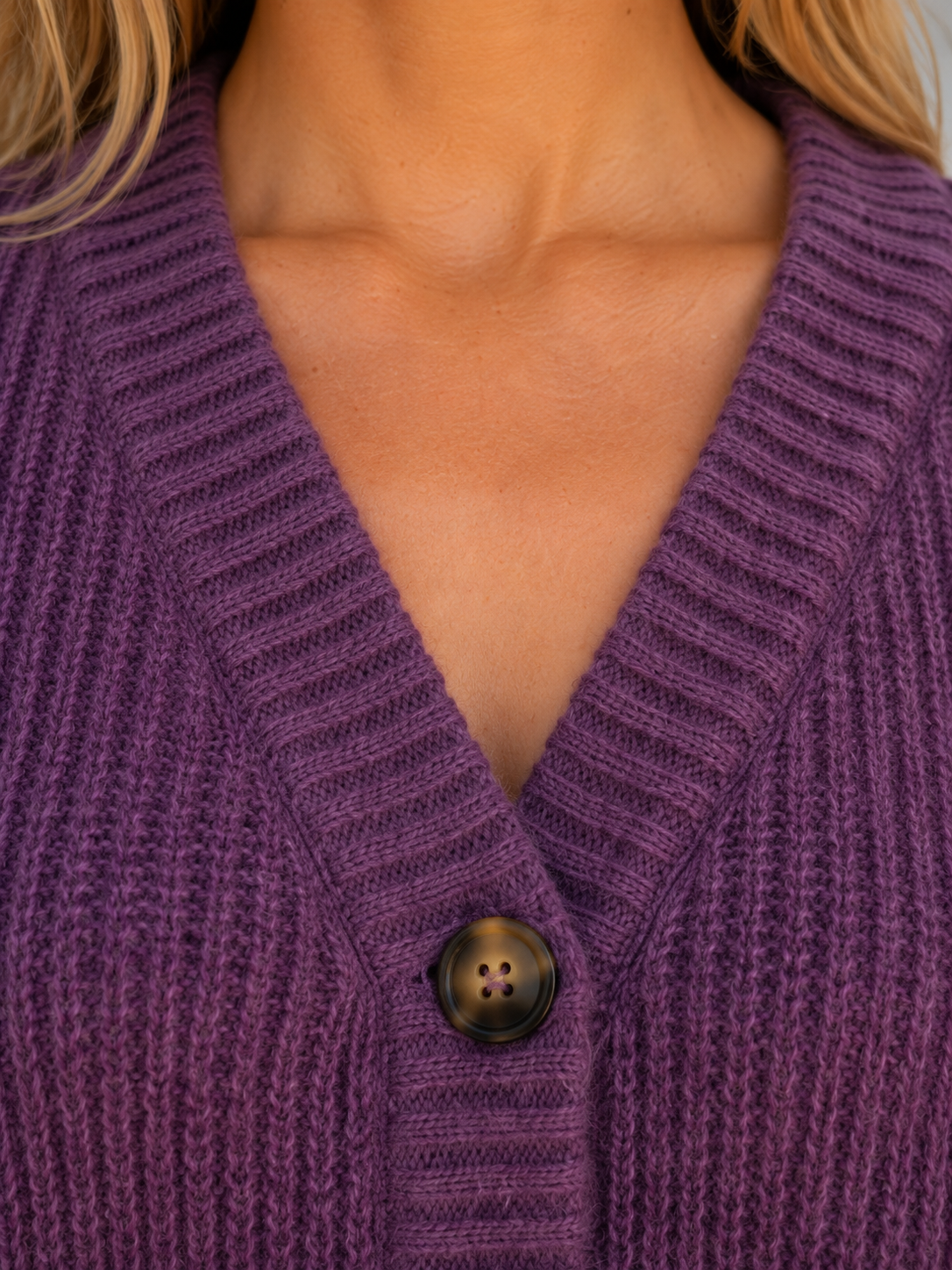 Woman wearing purple chunky knit ribbed cardigan with v-neckline and brown button closure