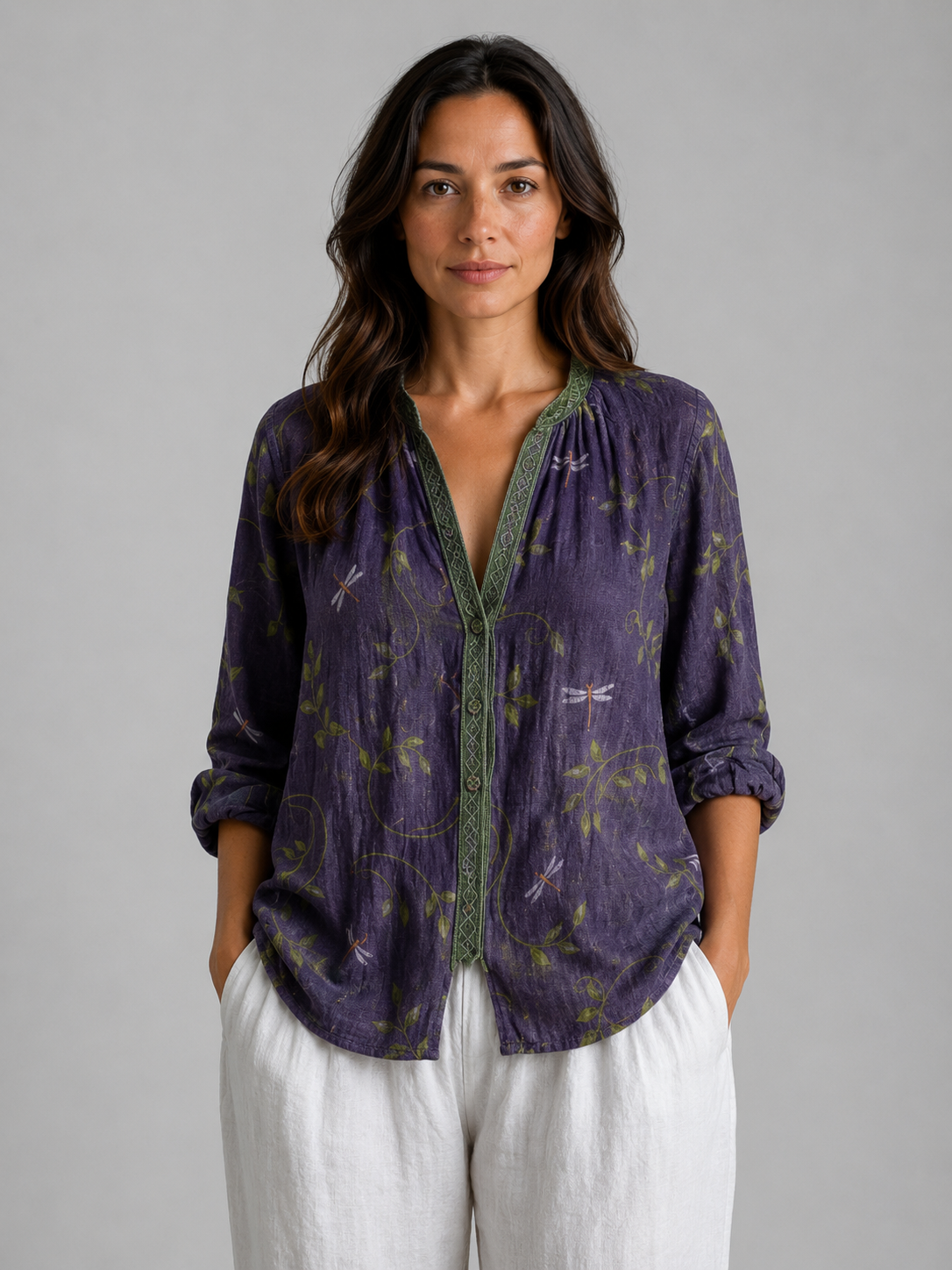 Woman wearing purple bohemian blouse with dragonfly print and green trim, paired with white linen pants