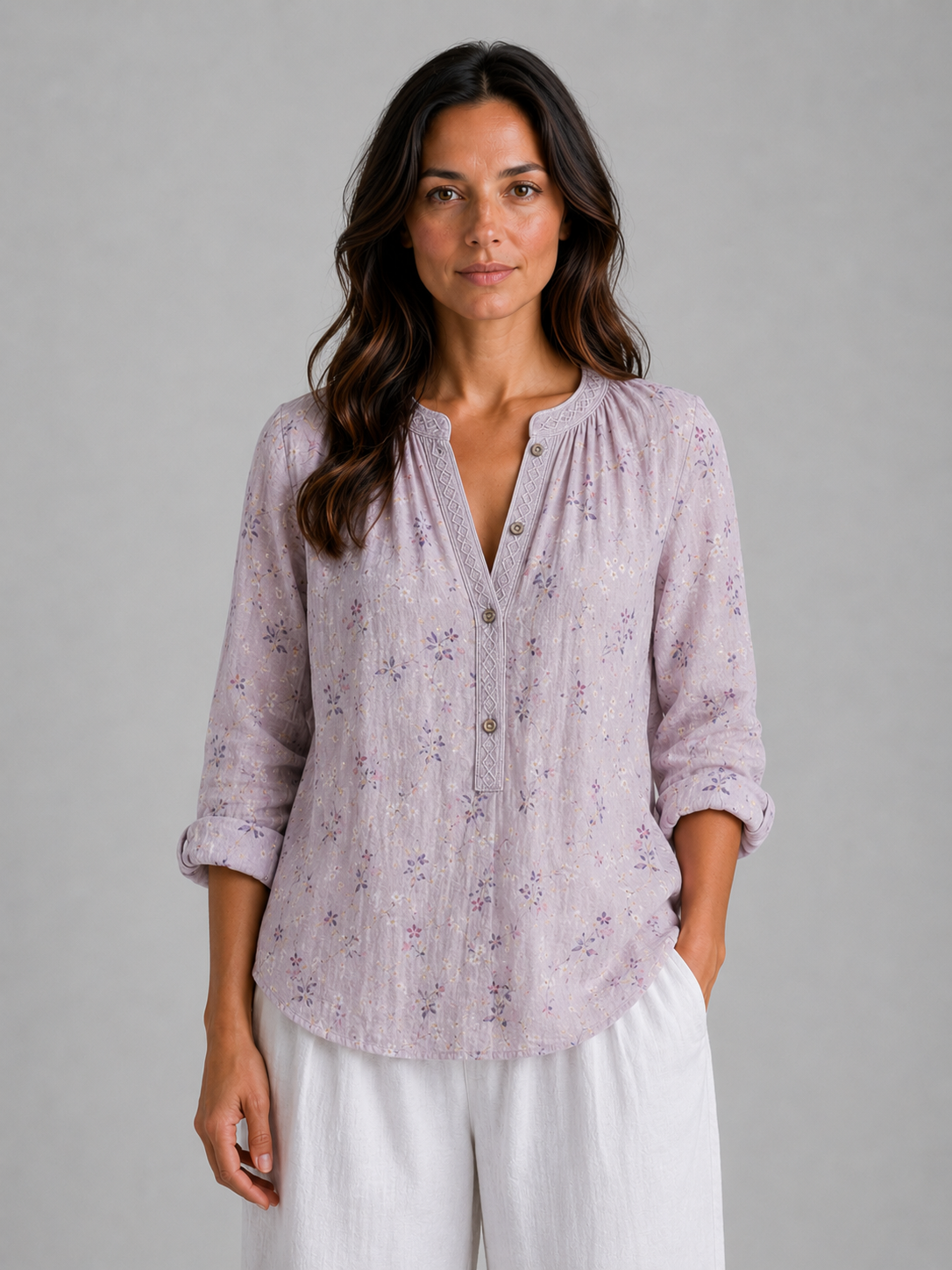 Woman wearing lavender floral v-neck blouse with button front and rolled sleeves, paired with white linen pants