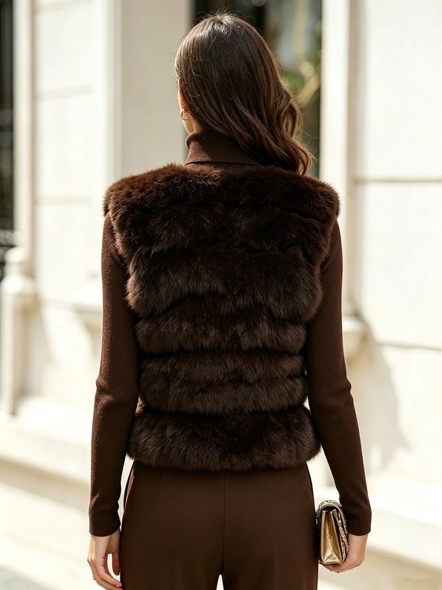 Woman wearing brown faux fur vest over matching turtleneck sweater, holding metallic clutch, standing outdoors