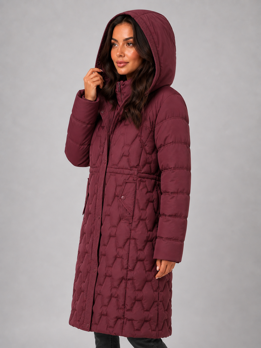 Woman wearing burgundy hooded quilted long puffer coat with full-length zip fastening, displayed against neutral background