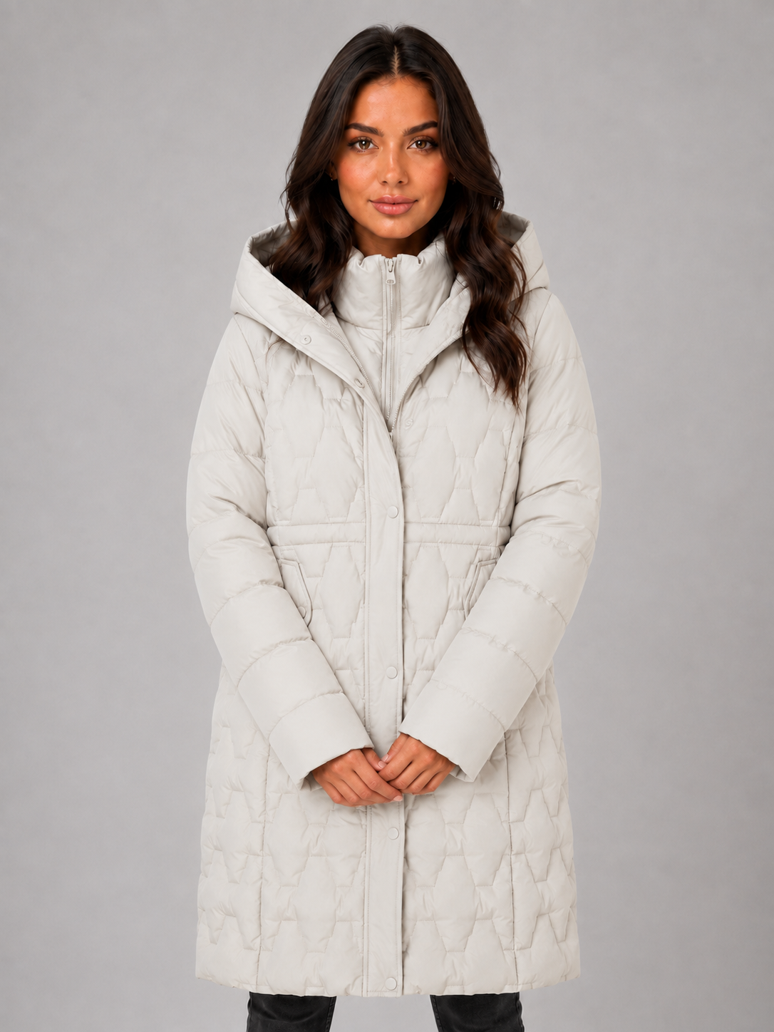 Woman wearing a cream white quilted long puffer coat with hood and full-length zipper, black pants visible below