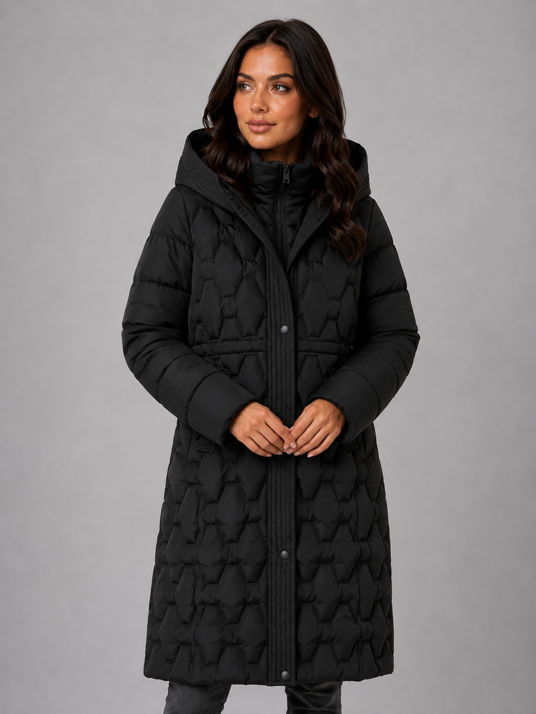 Woman wearing black hooded quilted long puffer coat with front zipper and snap buttons against gray background