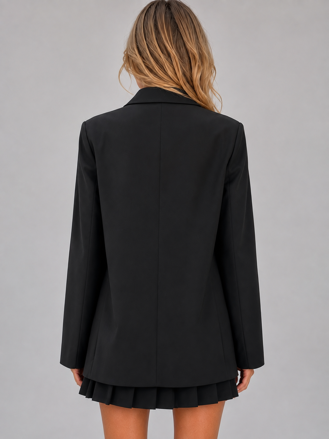 Woman wearing black oversized tailored double breasted blazer jacket with pleated skirt, back view