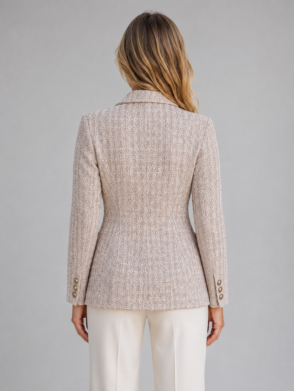 Woman wearing beige tweed double breasted blazer with white trousers, back view showing tailored fit and button details